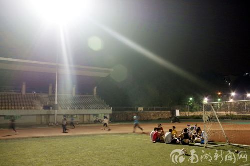 足球运动员们坐着休息，跑步的同学从他们身后跑道而过