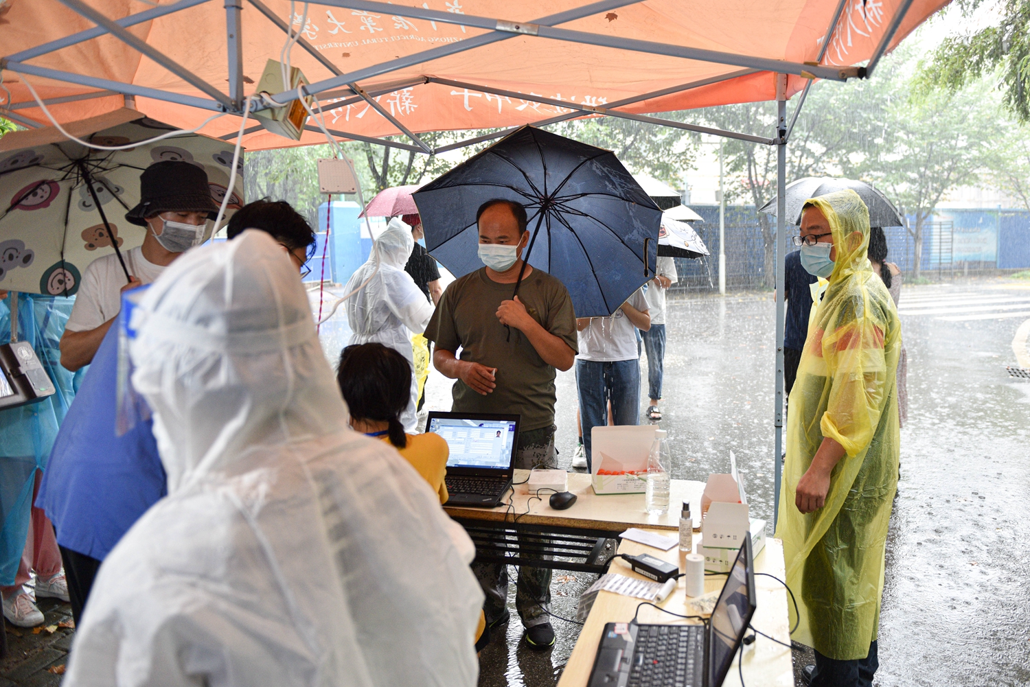 2021年8月10日，华中农业大学荟园检测点，学生志愿者在雨中为检测人员登记信息（学通社记者 段智为 摄）