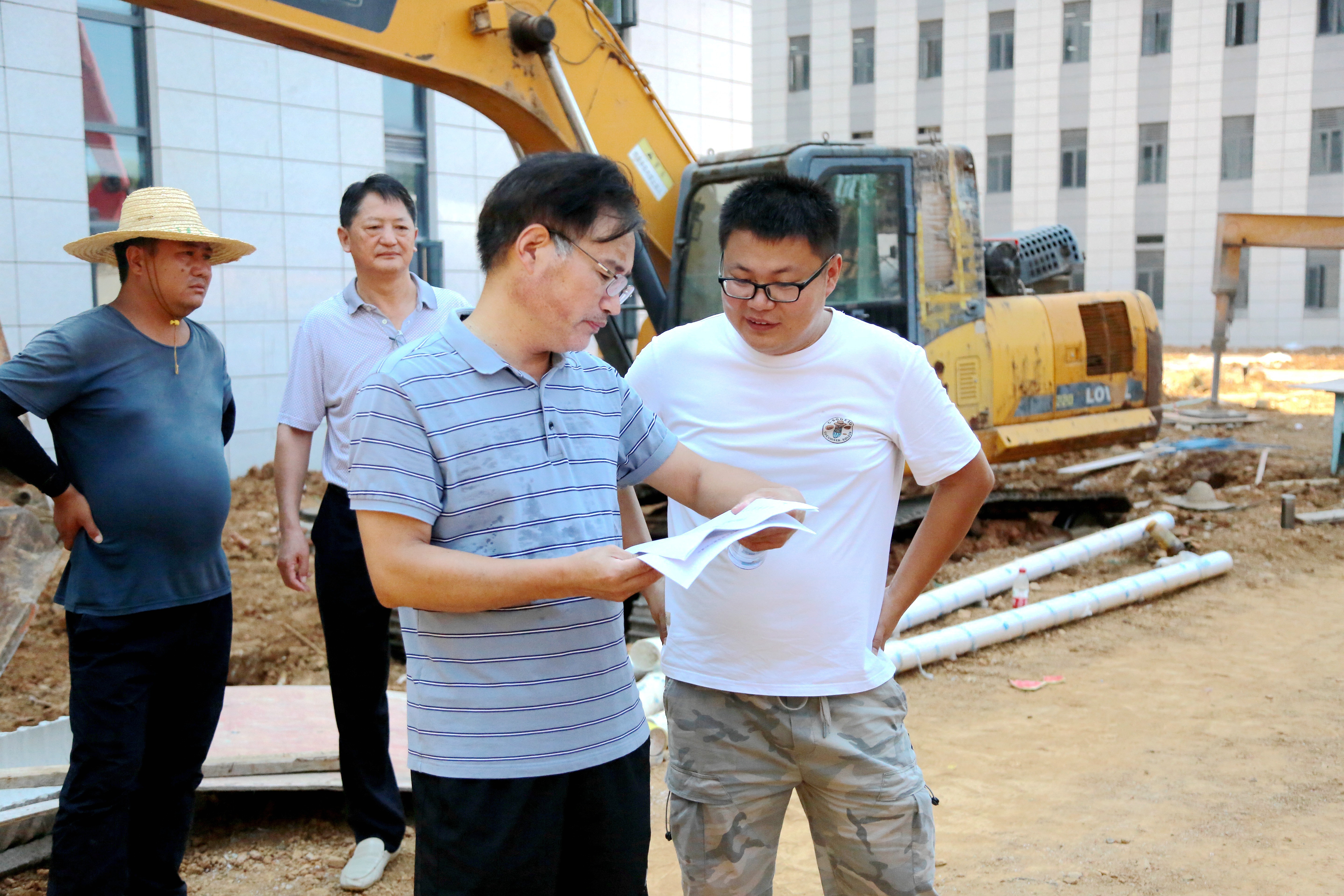 烈日下，建安部副处长秦长平与工作人员讨论项目施工情况（匡敏摄 )